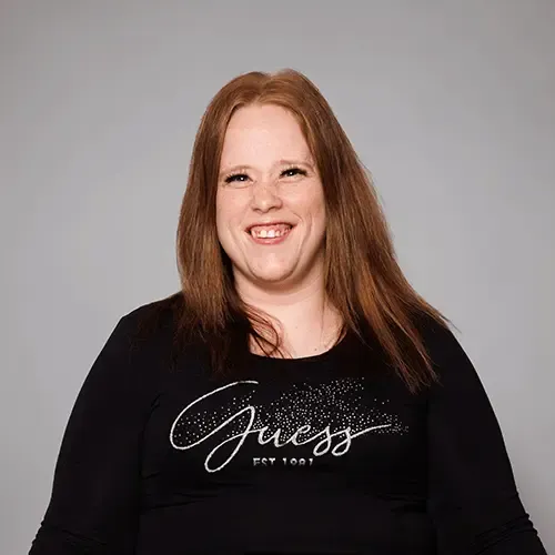 Melanie Wimmer mit langen roten Haaren, lächelnd, trägt schwarzen Guess-Pullover mit silbernem Schriftzug