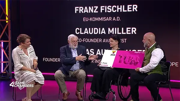 Dipl.-Ing. Dr. Franz Fischler übergibt den Magenta TUN Award an Claudia Miller und Andreas Ausserhofer von ava auf einer Bühne mit großem Bildschirm im Hintergrund